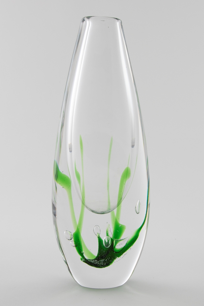 Flattrykket dråpeformet vase i klart glass med liten sirkulær munning. Dekor i grønt i underfangsteknikk, som minner om alger som vokser opp fra vasens bunn. En del luftbobler i glassmassen.