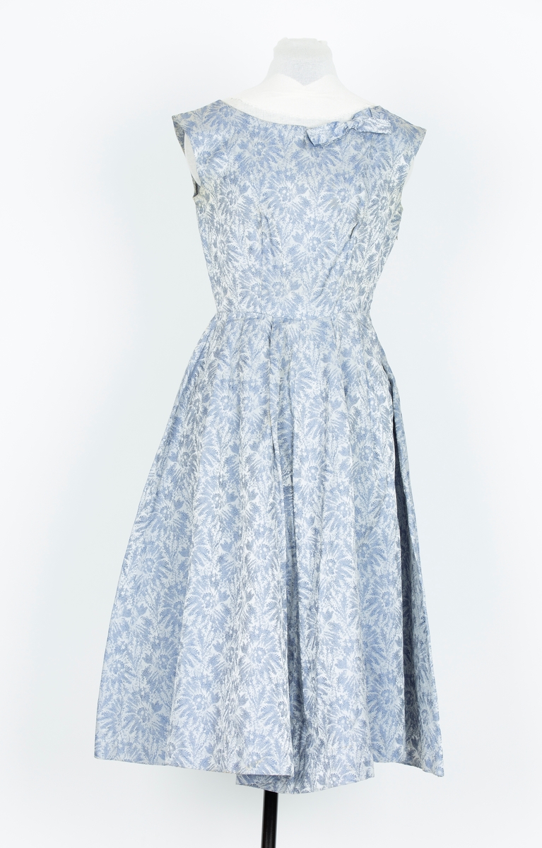 Selskapskjole. gråblå/blå brokade. Tettsittende lliv, lengdesnitt. Båtformet halsringing. Uten ermer. Pyntesløyfe av stoffet i halsringing. Skjørt i fire skrådde bredder lagt i legg mot livet, utskrådd wienerfold midt foran og bak.
Skjørtevidde nesten som rundklippet.

"Denne kjolen sydde jeg til bryllupet til Pers søster.svigerinne, våren 1956. Brukte den også i bryllupet til venninne St. Hansaften 1956 




kjortet er folde mot liv. Rund hals og uten erm. Glidelaas i siden. Sloyfe i halsen