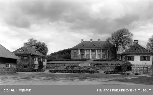 Exteriörbild av Rossareds herrgård vid Stensjön i Fjärås. Förlaga till vykort. Rossared är skriftligen känt sedan 1350-talet och ett av de gamla säterierna i norra Halland. Huvudbyggnaden fick sitt nuvarande utseende 1918 efter ritningar av göteborgsarkitekten Arvid Bjerke. Byggherre var ägaren skeppsredare Lars Gösta Dalman. Huset restes på grunden till den gamla manbyggnaden från 1884. Runt byggnaden projekterade Bjerke även terrassanläggningarna, som framgår tydligt på bilden. De två små flyglarna är symmetriskt placerade nere på den öppna gården.