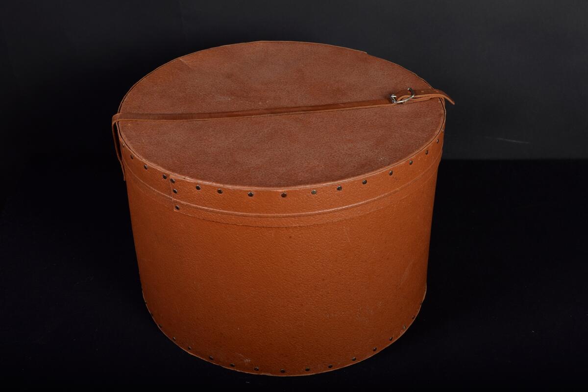 Hattask, av brun pressad papp, rund, läderrem att knäppa över locket och att bära i. Firmamärke: Pegasus. Alstermo Bruk. 