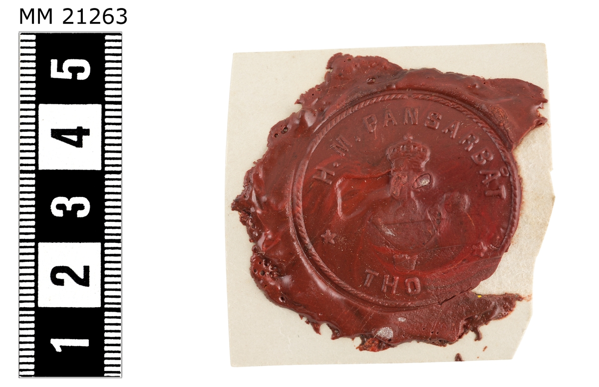 Sigillavtryck av rött lack på papper. I mitten krönt stockankare omgivet av tre kronor. Längs kanten text: "H.M. pansarbåt Thor".