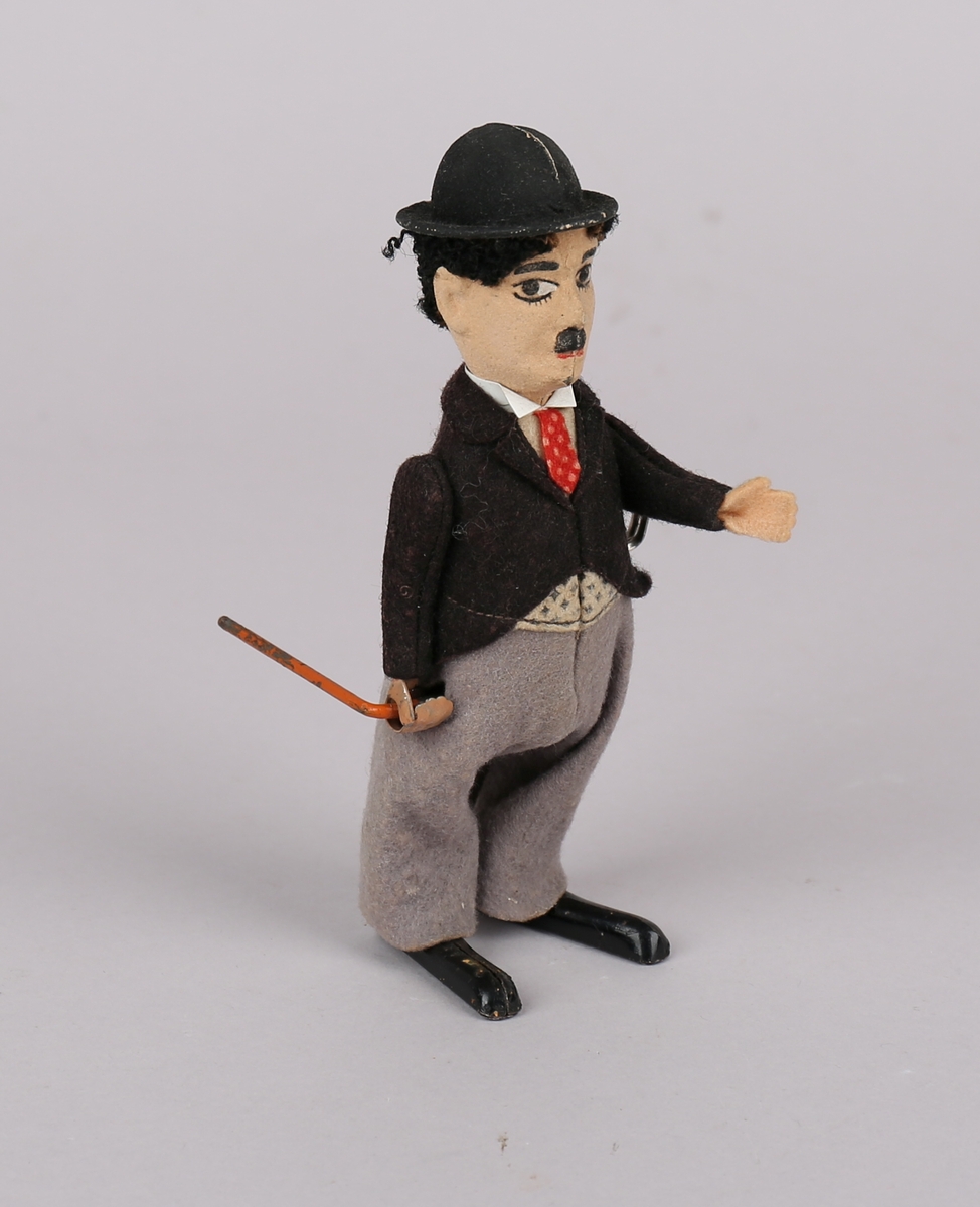 Mekanisk dukke utformet som Charlie Chaplin. Med stokk, bowlerhatt, slips, bukser og dressjakke.