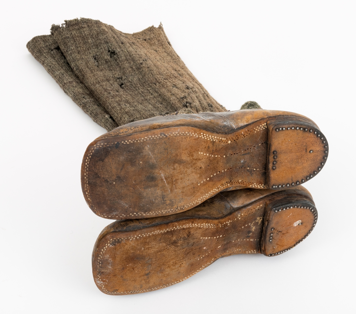 Støvlene er sydd av brunt lær.  Skaftene er strikket av grått ullgarn.  Sålene er plugget, hælene stiftet fast. 