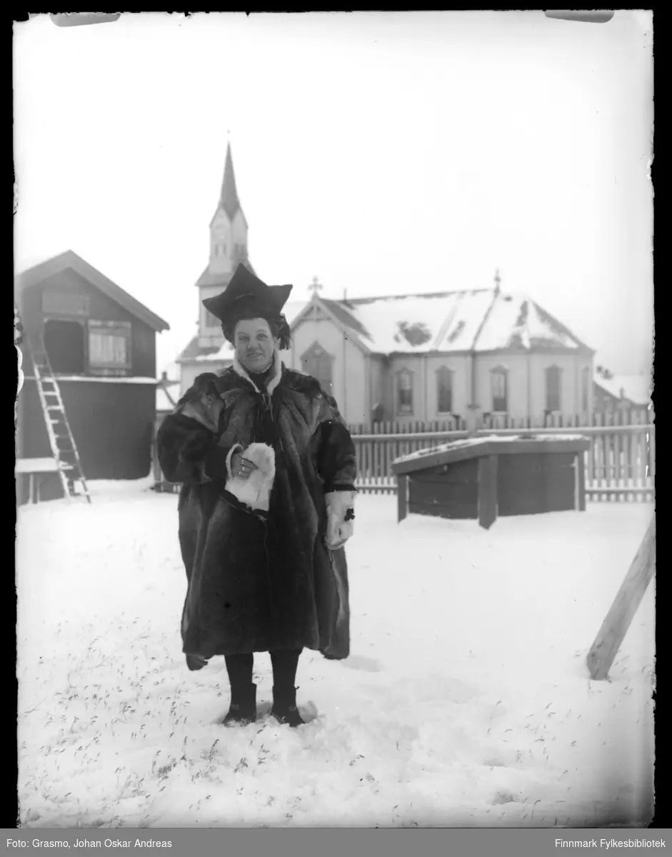 En person i pesk, stjernelue og skinnvotter fotografert ute i snø. Vardø kirke i bakgrunnen.