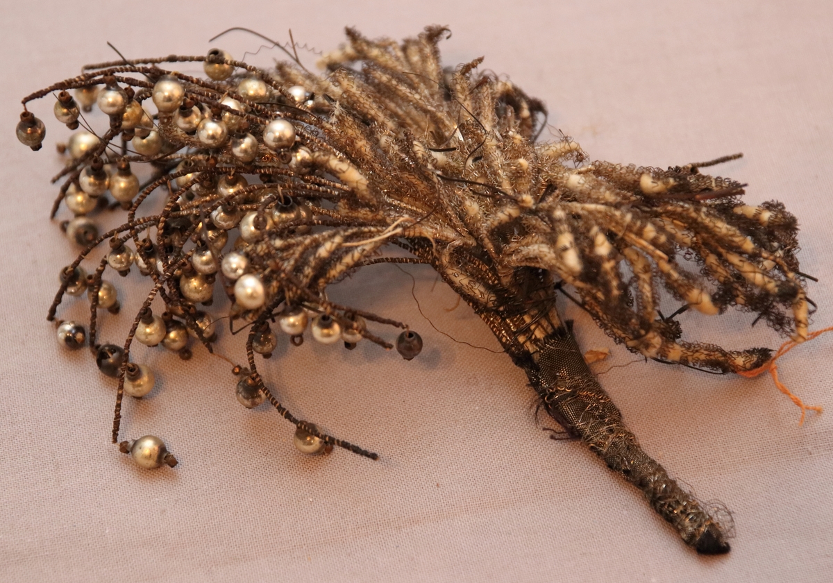 Hårprynad i form av ett knippe/bukett utformat av tråd, textil och med hängande silverpärlor.