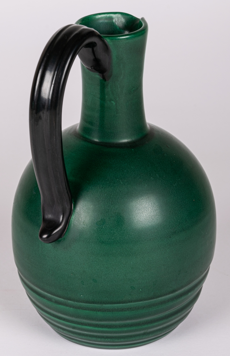 Likörkrus med pip och hänkel, lergods, modell 4346 av Eva Jancke-Björk, formgiven 1934. Glasyr MK, svartgrön matt glasyr som användes åren 1934-1937.