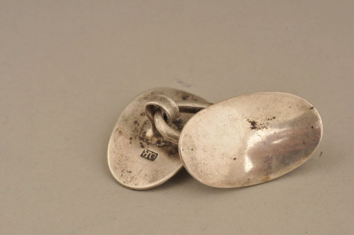 To ovale og konkave knappar sett saman med ei lykkje. Stempla på undersida.