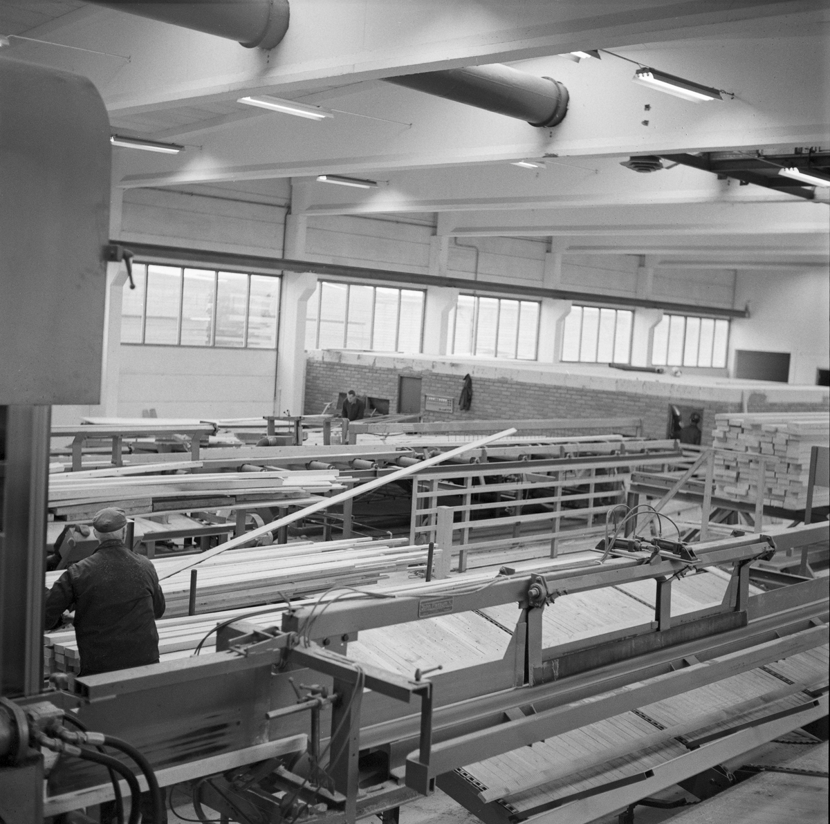 Industrilokale for trelastproduksjon ved Trysil kommunale Sag og Høvleri i Hedmark, høsten 1970. I 1970-71 ble denne bedriften modernisert for 3,7 millioner kroner, som på denne tida var et meget betydelig pengebeløp - en god del større enn hva lokalpolitikerne hadde akseptert da de stilte seg bak moderniseringsprosesessen. Målet var å sikre lokal foredling av mest mulig av det tømmeret som ble produsert i Trysil, og å bidra til å skape industriarbeidsplasser i skogsbygda. Den nye bygningsmassen ble oppført av betongelementer, både for å oppnå tilfredsstillende soliditet og fordi dette var brannresistente materialer. Dette fotografiet er muligens fra det nye høvleriet, som fikk ei grunnflate på drøyt 1 000 kvadratmeter. 

Mer informasjon om det nye sagbruket som ble reist i Trysil ved inngangen til 1970-åra er gjengitt under fanen «Opplysninger».