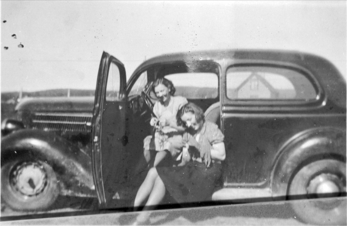 To kvinner sitter og strikker i døråpningen på en bil.
