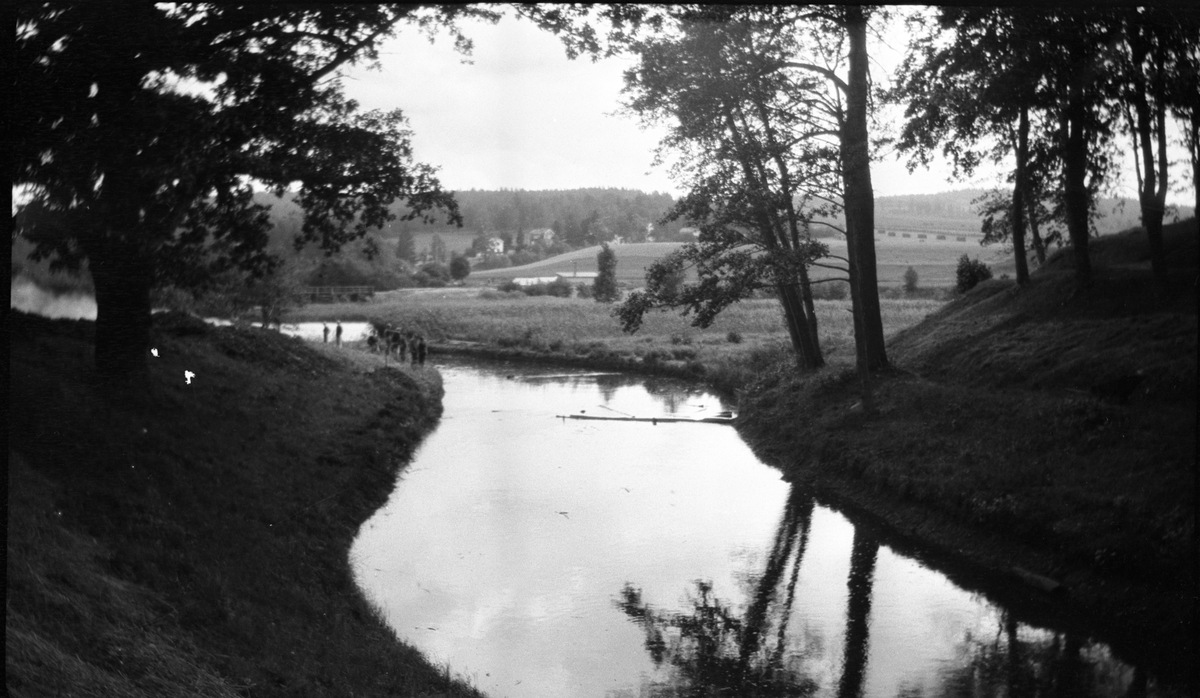 Foto taget i samband med de arkeologiska undersökningarna vid Rumlaborg sommaren 1935. Till höger skymtar borgkullen och längre fram hur den inre vallgraven är förbunden med Huskvarnaån. Arbete pågår vid sydsluttningen av den inre vallen.