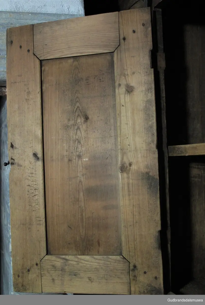 Lite innebygd skap i stue fra 1700-tallet. Skaprom delt av hylle på midten. Dør og skapramme er tappet og med treplugger gjennomtappene. Malt i brun, rød og grønn, en fargebruk som ble vanlig fra slutten på 1700-tallet.