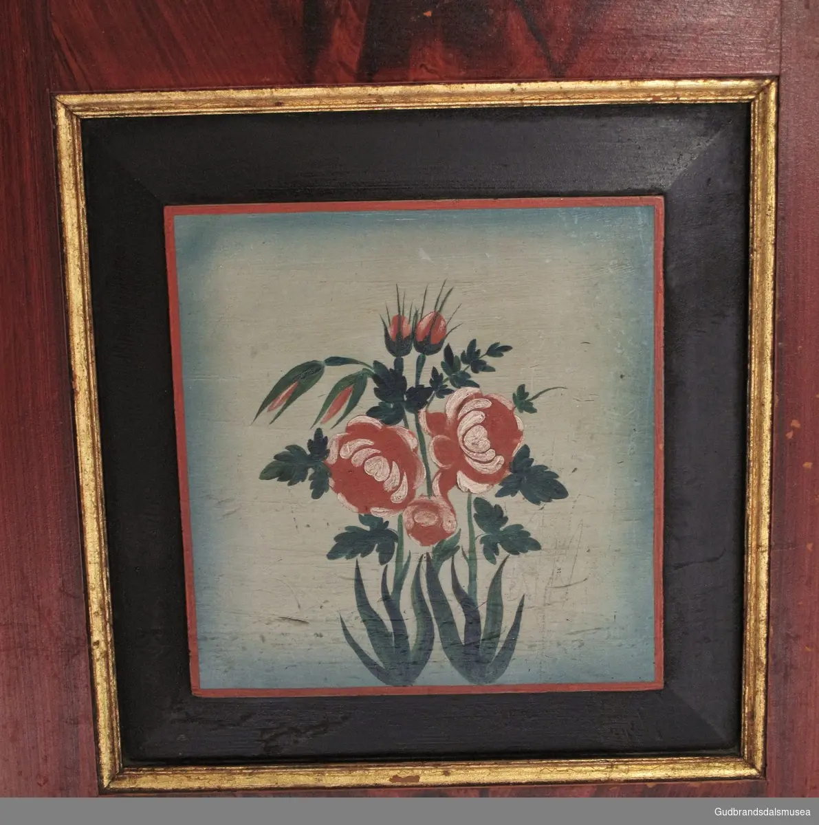 Naturalistiske roser røde og hvite roser med gønnt bladverk, rammet inn med rød kant innerst etterfulgt av en bred svart kant og ytterst en kant i gull. Bakgrunn lys blå.