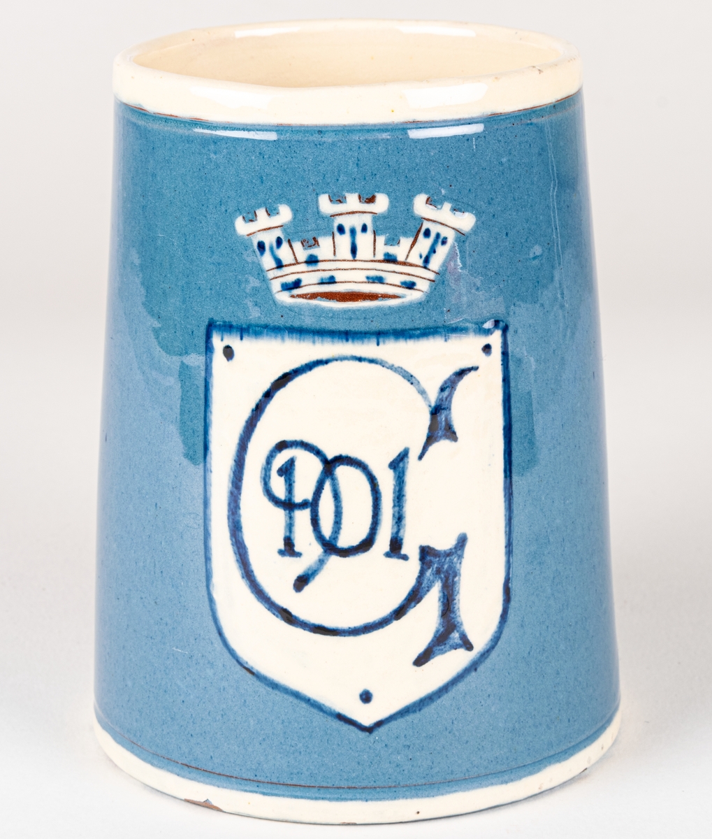 Ölsejdel av keramik. Utsidan glaserad och försedd med vapensköld i vitt med mörkt blå text: G 1901. Insidan vitglaserad. Över skölden en krona. Tillverkad som souvernir för Gävleutställningen 1901.