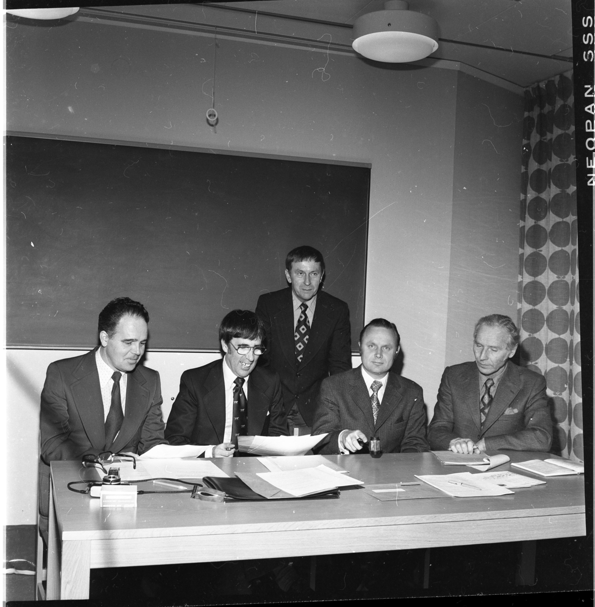 Fyra kostymklädda män sitter vid ett bord med papper framför sig, en håller en ordförandeklubba i handen. En femte man står bakom dem. De är sittande fr v: Ingemar Lago, Tom Sonesson, Allan Svensson samt Edvin Tollén.