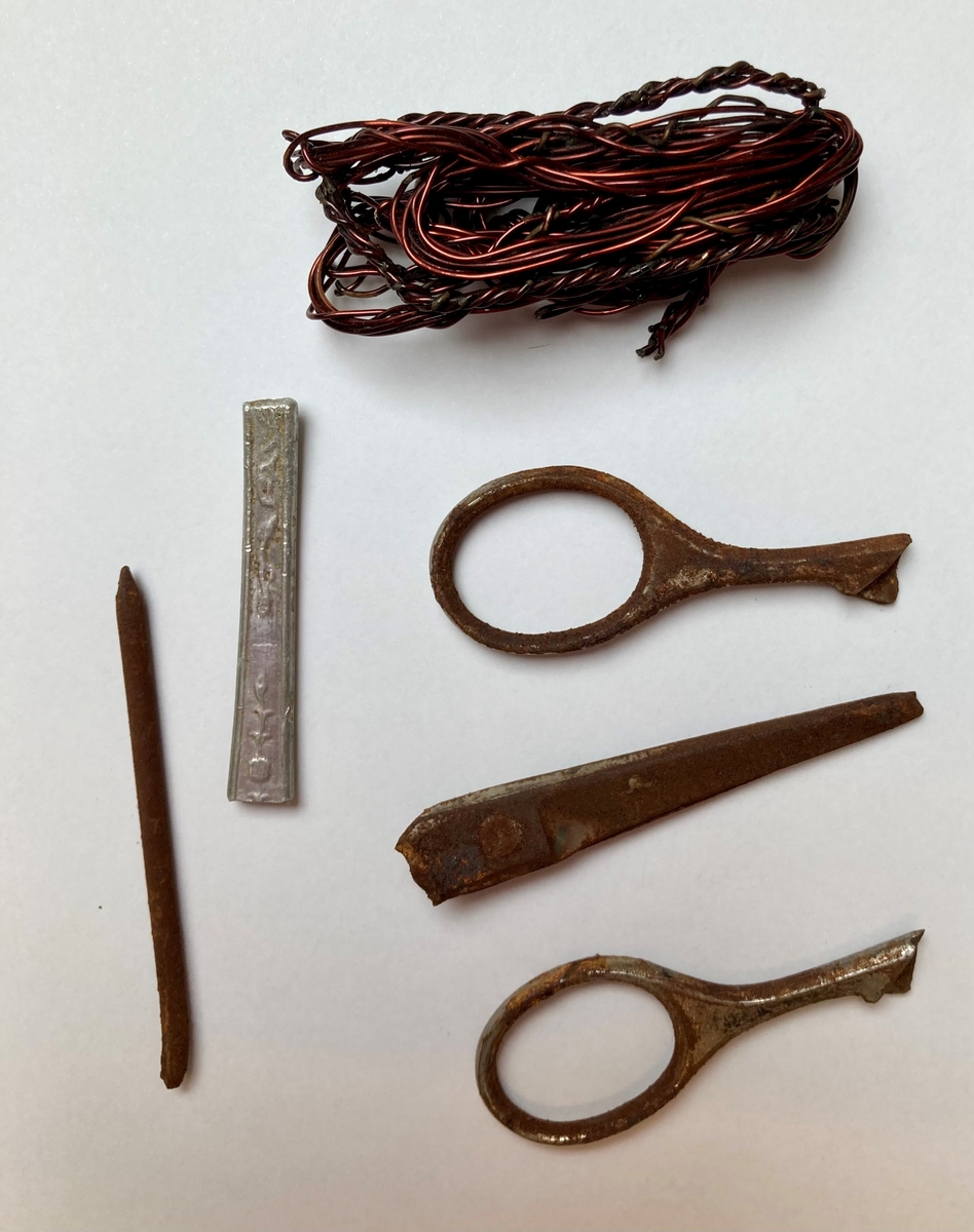 Seks metallobjekter; en klump sammenfiltret ståltråd, en liten saks i tre deler, en spiker og skaftet av en teskje.