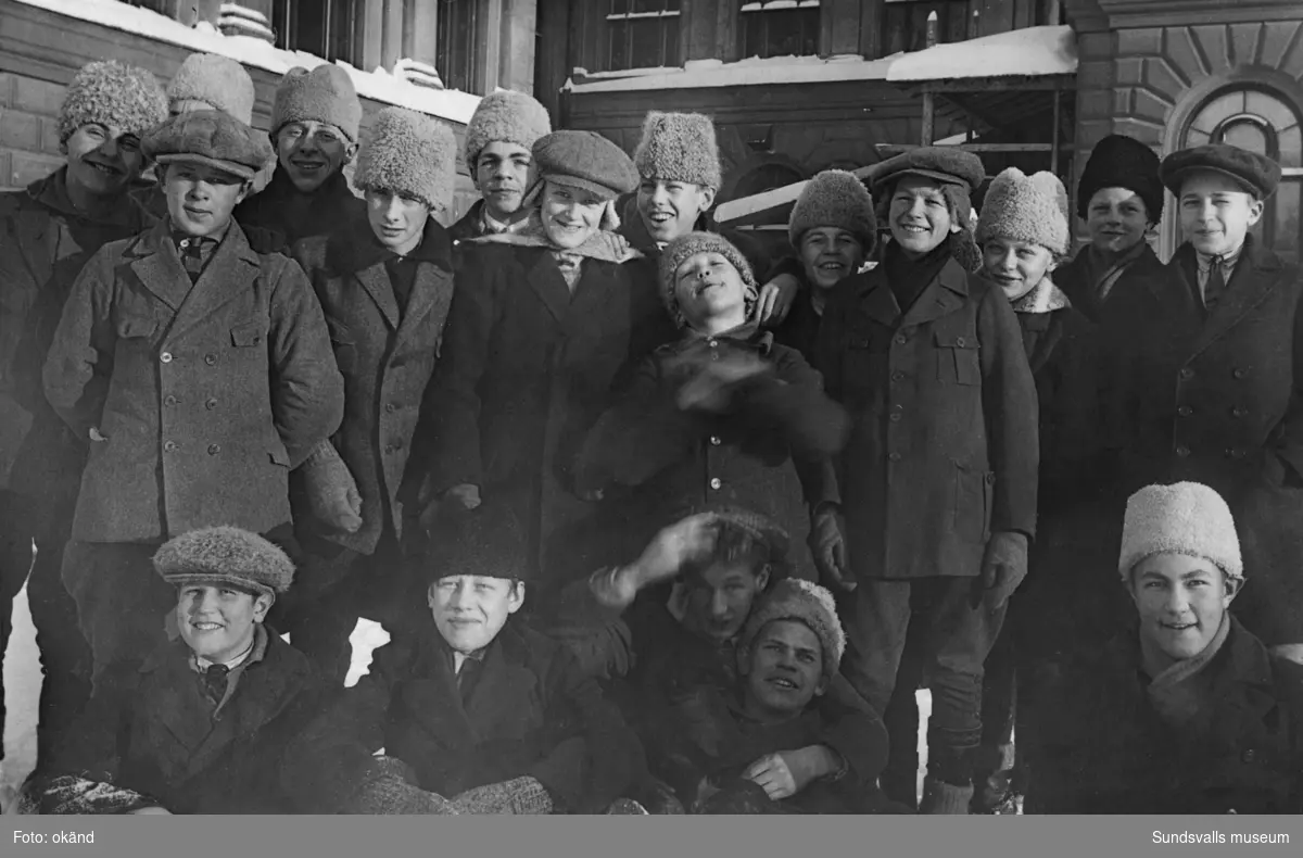 En grupp med 19 glada pojkar i vintermössor på Läroverkets baksida. På bildens baksida står: 5a den 6 febr 1926 (i 30 graders kyla). Ur en samling som tillhört Margareta Bergman, Nacksta.