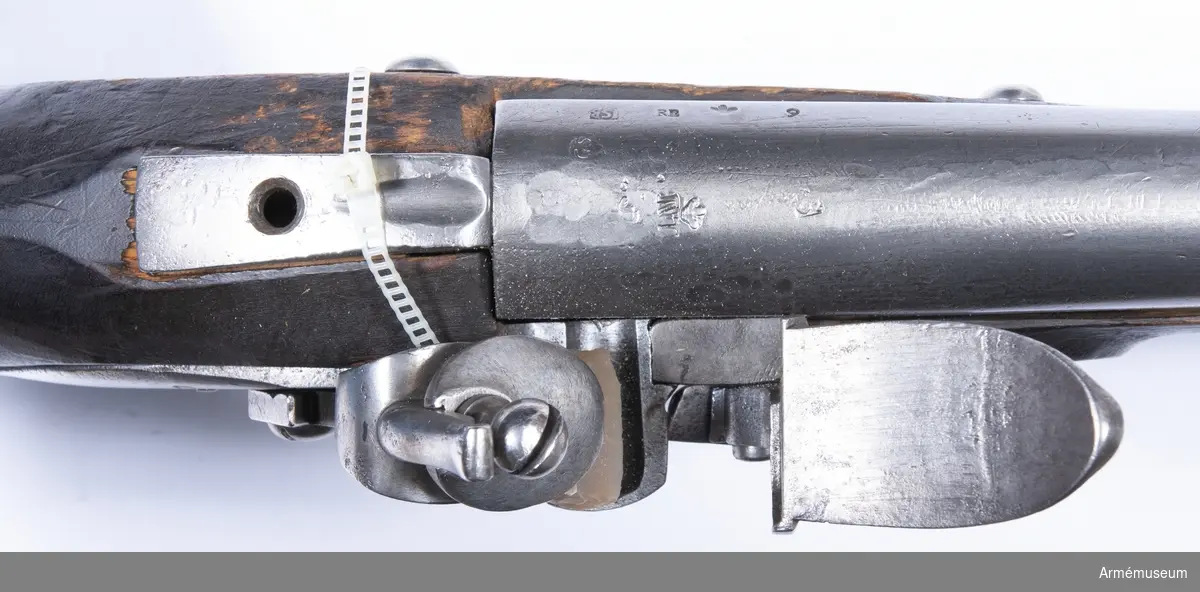 Grupp E II.
Gevär med flintlås.
Kal. 20,3 mm. Sannolikt reparationsmodell från 1700-talets slut. Sammansatt av delar till äldre gevär. Laddstock av järn. Varhaken saknas. Pipan tillverkad i Norrtälje. Märkt "2" över "86", en punkt och "6."