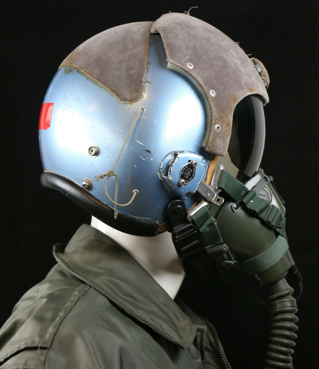Blå metallic hjelm med grå filt og rødt reflekstape i nakken formet som et + 