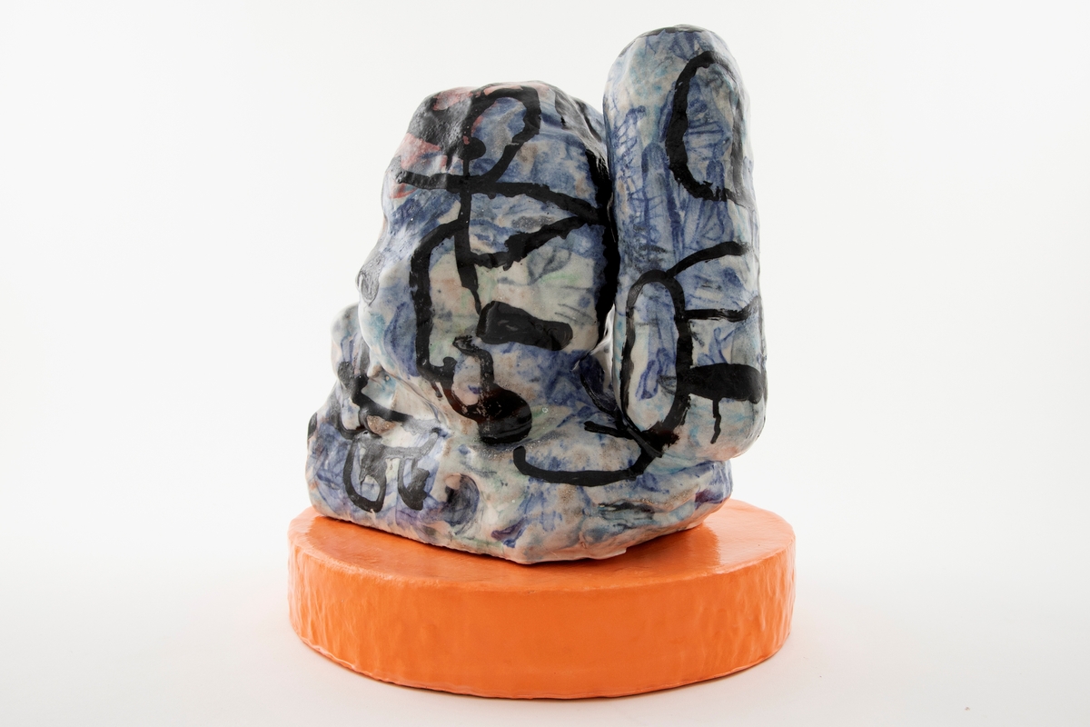 Skulptur i to deler. Frittstående abstrakt skulptur med blå, rosa og hvit glasur med svart nonfiguraiv glasurtegning. Skulpturen står på oval oransje base.