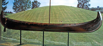 Bildet viser en kopi av Osebergskipet foran gravhaugen.. Foto/Photo