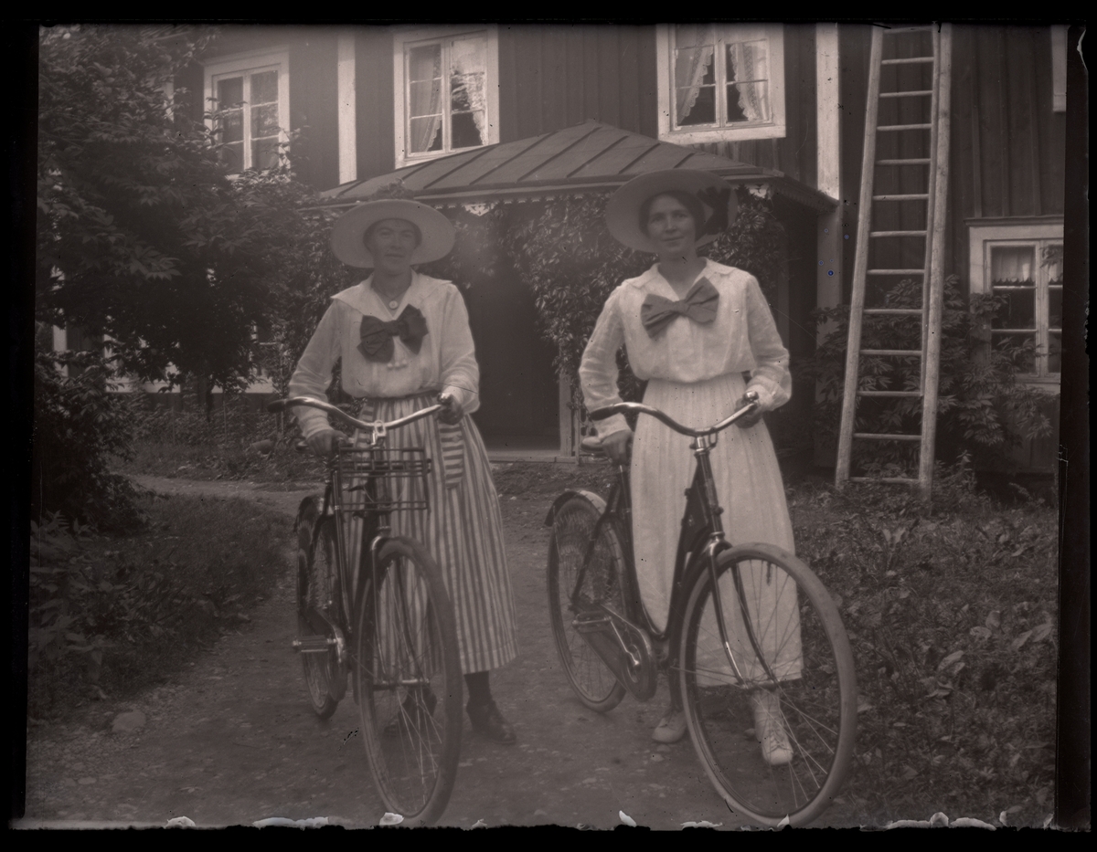 Grupporträtt, två kvinnor med cyklar, framför gården.