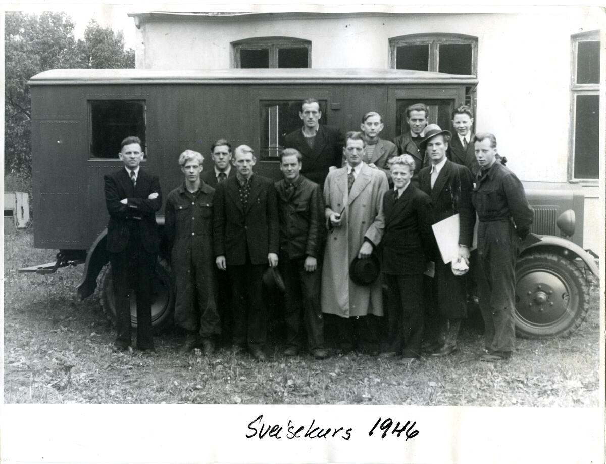 Sort-hvitt bilde av gruppe med menn foran gammeldags buss