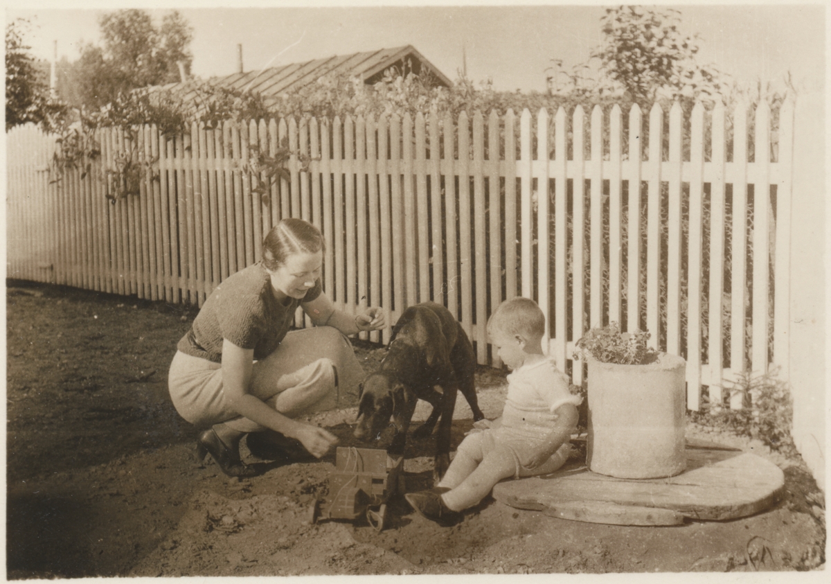 Kvinne, hund og gutt fotografert ved stakittgjerde.