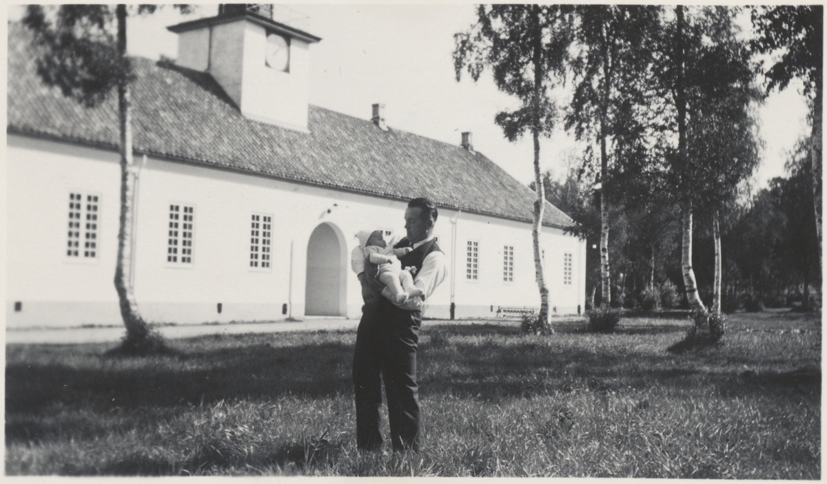 Birger Falstad med sønnen Tore Falstad (f. 1934) på armen foran murbygningen på Falstad skolehjem på Ekne i 1934. Birger Falstad var ansatt på skolehjemmet, og familien bodde i denne bygningen i flere år.