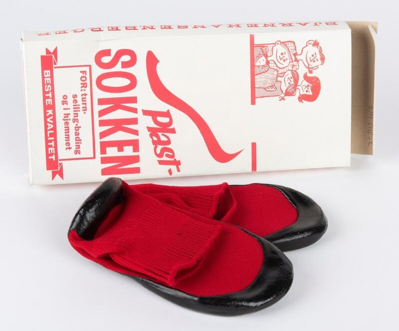 Bildet viser et par røde sommer med sort gummi under på sålen. Bak ligger en hvit eske med rød skrift. Det står plast sokken (Foto/Photo)