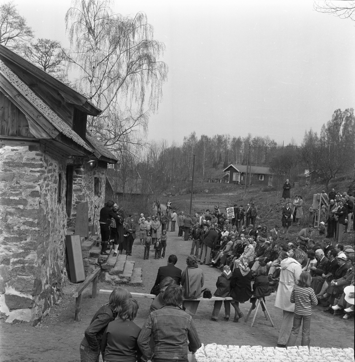 En folksamling kring Rasmus kvarn i Röttle. Två spelmän på trappan till kvarnen. I förgrunden står ett bord med mjölpåsar.