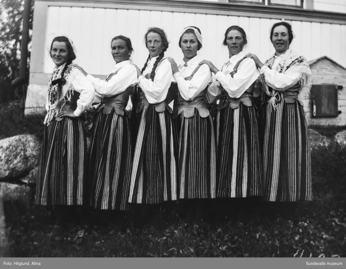 Kvinnor i Medelpadsdräkt. På första bilden är det, från vänster, Irma Edberg, Ada Wiström, Greta Larsson, Märta Björk, Adelia Larsson och Hilma Höglund. På andra bilden finns även tvillingflickorna Ingrid och Irma Höglund med.