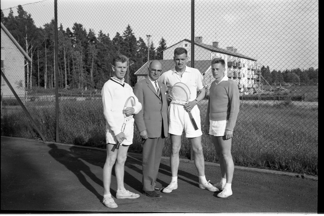 Tre tennisspelare och en kostymklädd man på en tennisplan.