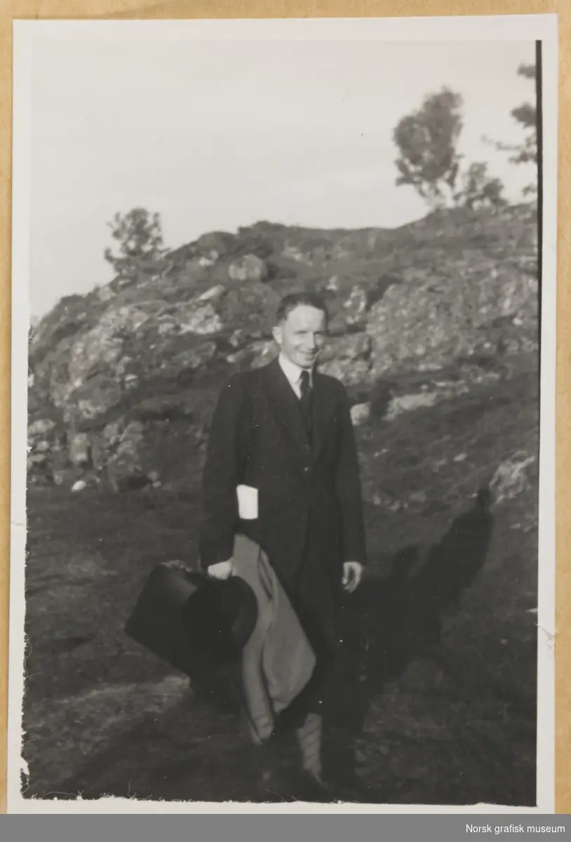 Utendørsmotiv, en mann står foran en fjellknaus. Han er kledt i dress og slips, med veske og frakk i høyre hånd. Navn ukjent. Fotografert i forbindelse med Vestlandsk Trykkerstevne i Bergen 1946.