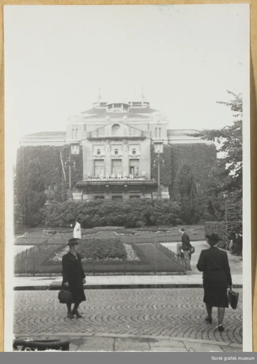 Utendørsmotiv. Bygningen Den Nationale Scene i Bergen ses i bakgrunnen, med parkanlegg og mennesker i forgrunnen. På fasaden reklameres det for forestillingen "Carmen". Fotografert i forbindelse med Vestlandsk Trykkerstevne i Bergen, 1946.