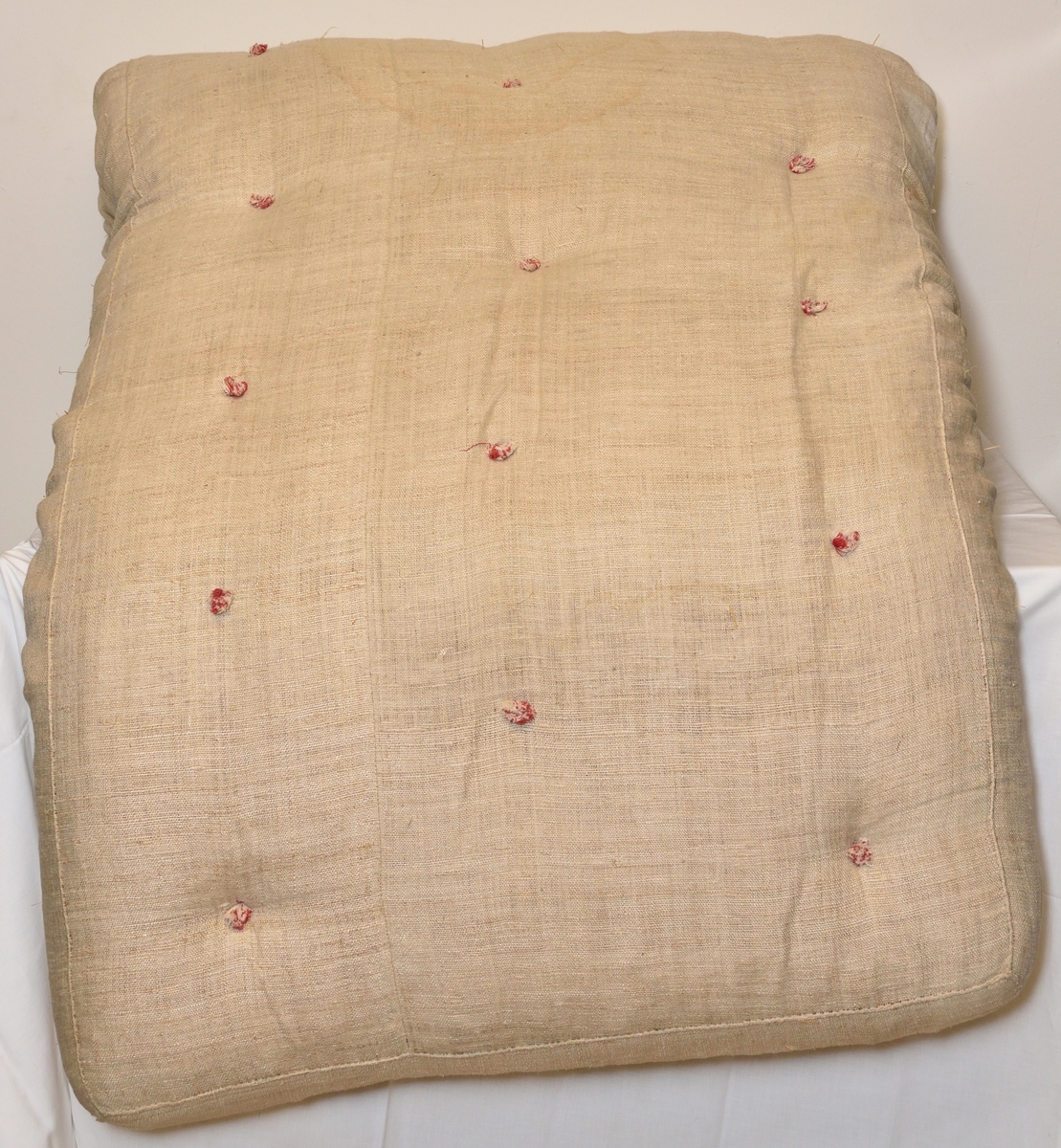 Madrass tillverkad i grovt lingarn, med halmstoppning. Puskor i rött och vitt garn.