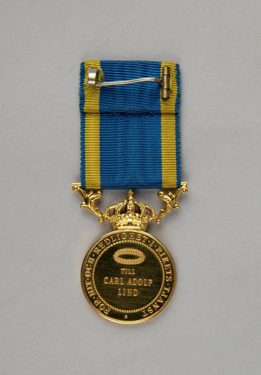 Guldmedalj (:1) i ask (:2). 
Medaljen pryds av Gustaf V:s profil på ena sidan med texten "GUSTAF.V.SVERIGES.GÖT-O-VEND.KONUNG", konsnärens initialer ingraverade under porträttet "AL".  På den andra sidan står det "FÖR.NIT.OCH.REDLIGHET.I.RIKETS.TJÄNST TILL CARL ADOLF LIND". Medaljens rundel kröns av en kunglig krona. 
På medaljen är fäst ett blågult band för fastsättning.
Medaljen ligger i en röd ask. Insidan av asken är klädd med lila textil. Asken har ett litet mässingslås.
