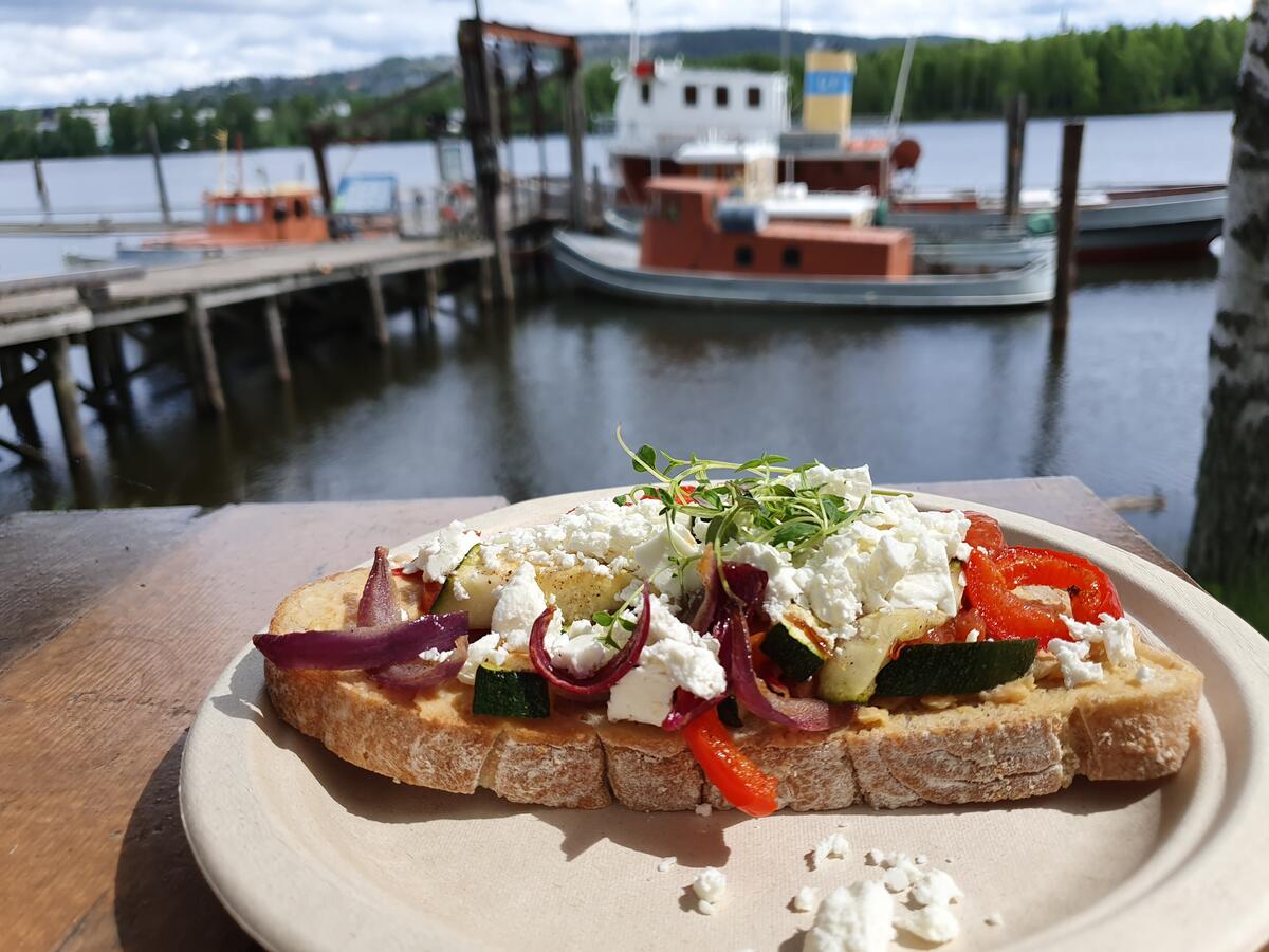 Foto av mat på tallerken på bord med brygge og båt i bakgrunnen.