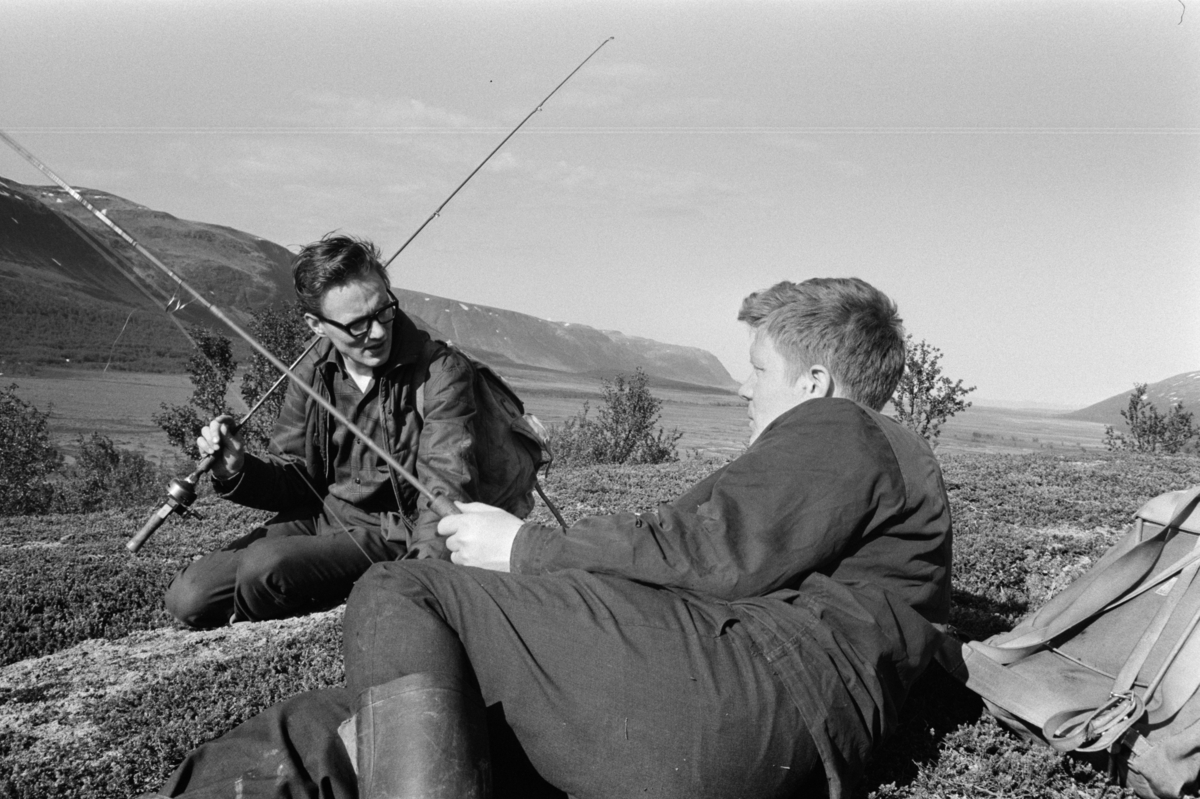 To karer med fiskestenger slapper av foran elvelandskap.