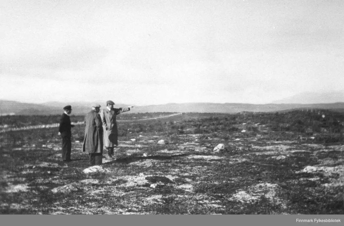 Tre menn står på Karasjokfjellet å ser utover vidda. Et stykke bak dem ser man riksveg 930.