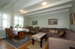 Interiør med sofa, bord med seks stolar, måleri på veggane