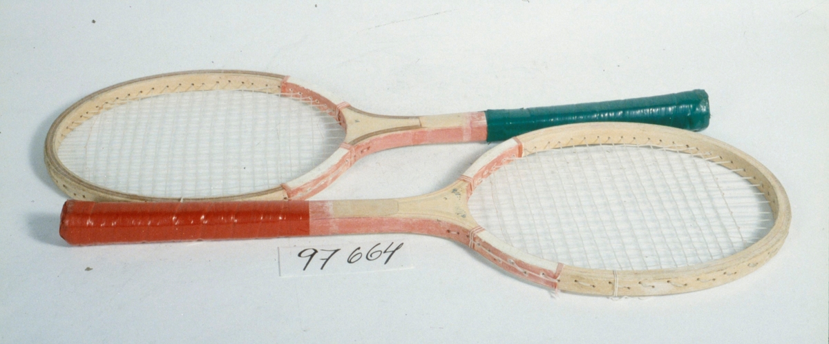 Ett par badmintonracket, av trä samt flätat nylonsnöre. Runt skaften är röd respektive grön plasttejp virad.