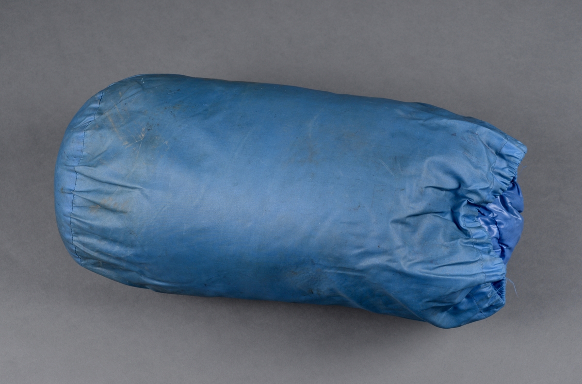 En sovepose i trekk/pose av merket Ajungilak (Nanok Babyble 4000). Soveposen har yttertrekk av blått kunststoff og er foret med oransje bomullsstoff. Soveposen er fylt med dun. Langs åpningen er det en løpekant der det er tredd i bomullsbånd for stramming. På snoren er det en enkel plastlås. På soveposen er det også snorer for å knyte rundt posen når den er rullet sammen. Til posen er det et blått nylontrekk med snøring i åpningen og en enkel plastlås for lukking. På soveposen og på trekket er det sydd på identiske merker, se "Påført tekst/merker".