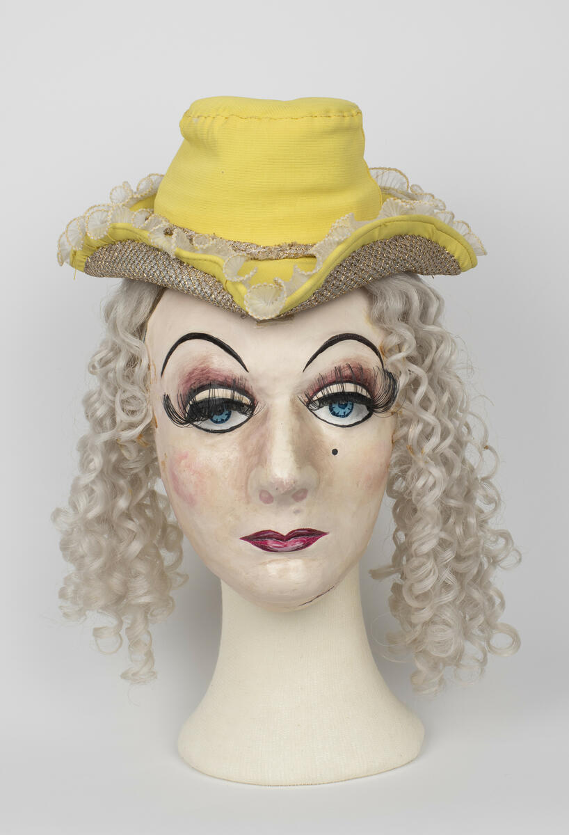 Dubbelmask med hatt och hår använd för rollen "Baronessan" i uppsättningen ”Pierrot i parken”.
Masken består av en halvmask som bärs över ansiktet och en ansiktsmask som bärs över bakhuvudet. Hatten och håret sitter fast i masken.