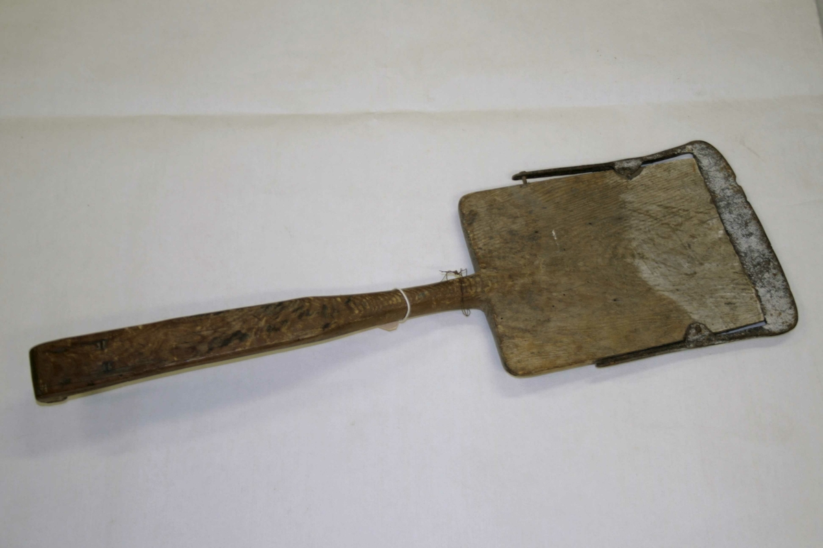 Liten jernskodd spade i tre med kort skaft, spadebladet er flat rektangulær, laget i ett sammenhengende trestykke, øverst på håndtaket forsterket.