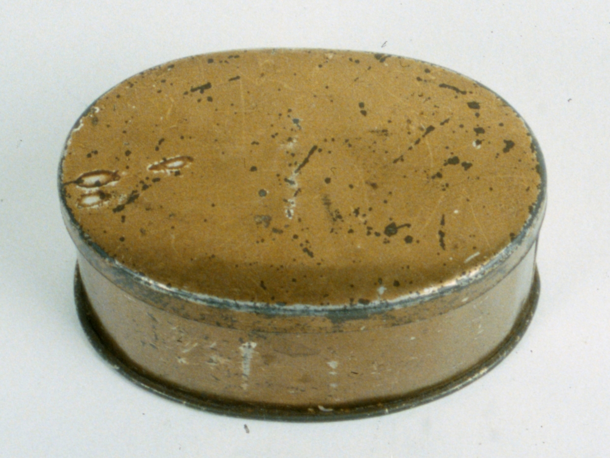 Oval guldfärgad ask med lock innehållande häftstift.