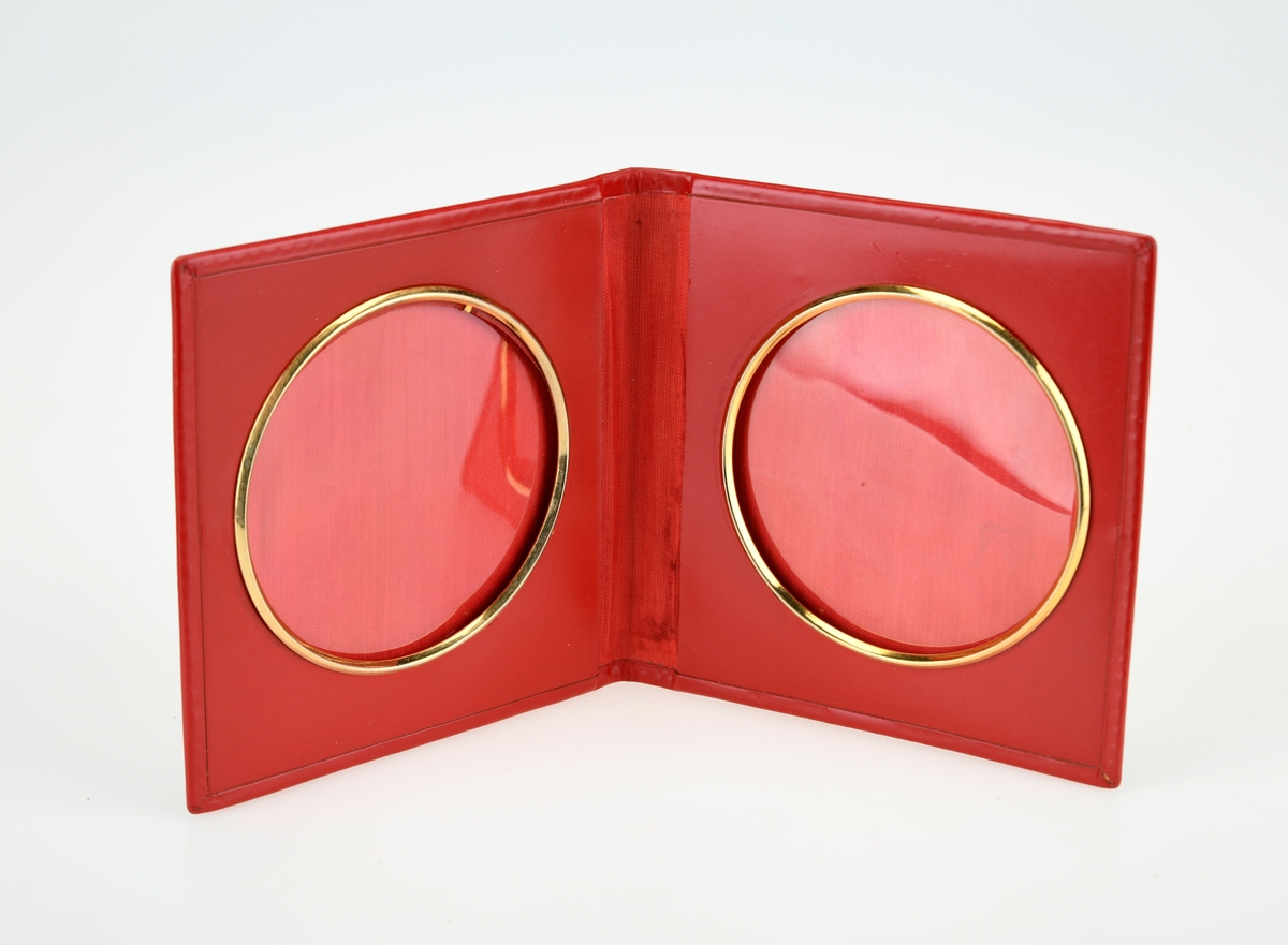 En folderamme med plass til to bilder. På utsiden er rammen i rødt skinn, mens på insiden er den kledd i et rødt stoff. Bildefeltene er sirkulære, og er omringet av en ring av forgylt metall. Bildene er dekt med gjennomsiktig plast.
