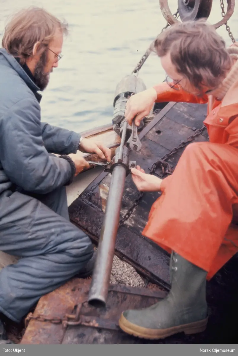To menn arbeider med et stålrør på dekk på ei treskute, antageligvis "MS Gulafjord".