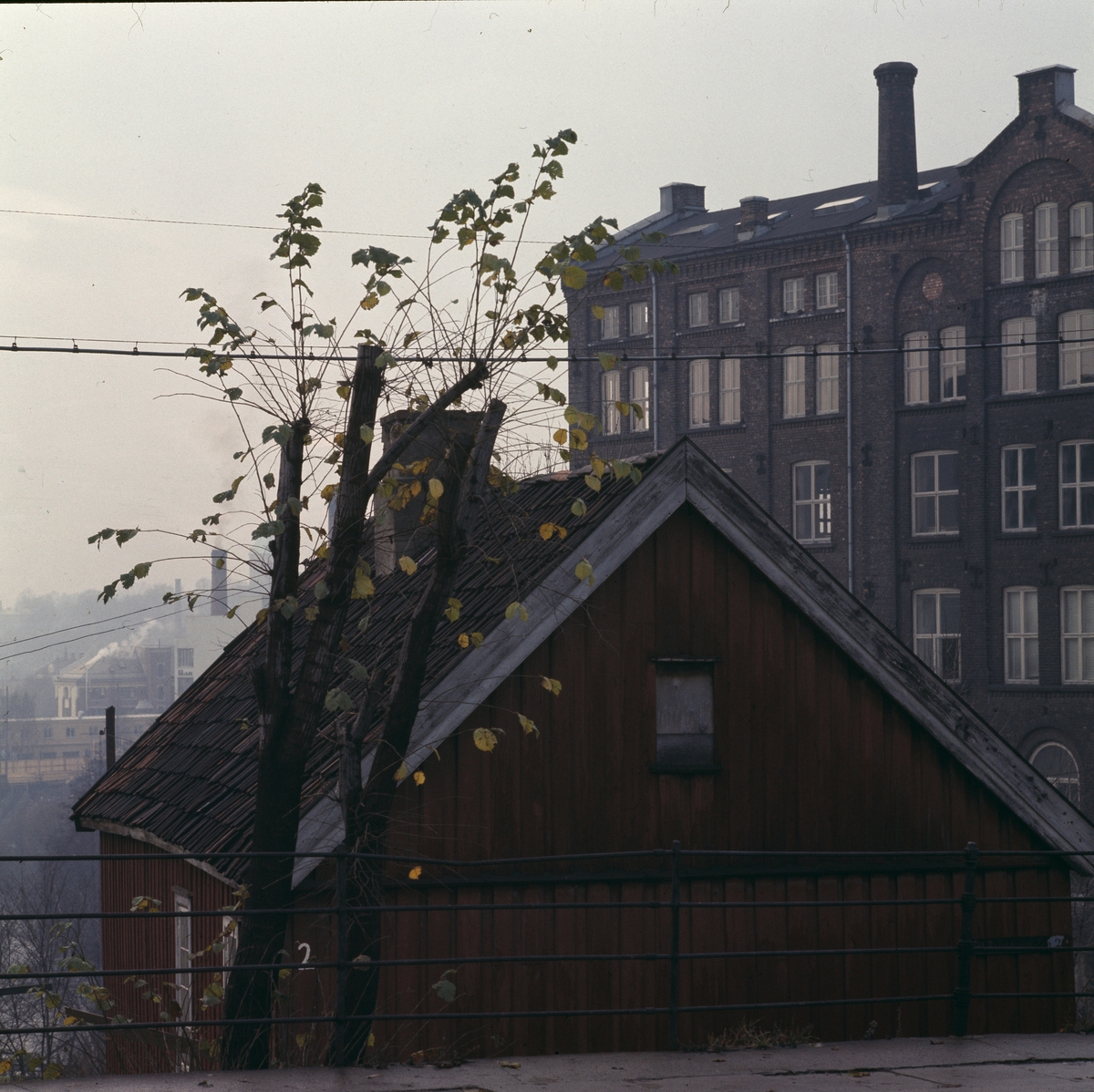 Bygninger ved Beyerfoss ved Akerselva fotografert i november 1976. I forgrunnen et lite trehus, nå "Hønse-Lovisas" hus. I bakgrunnen sees fabrikkbygninger tidligere brukt av Hjula veveri og Knut Graahs veveri og spinneri. 