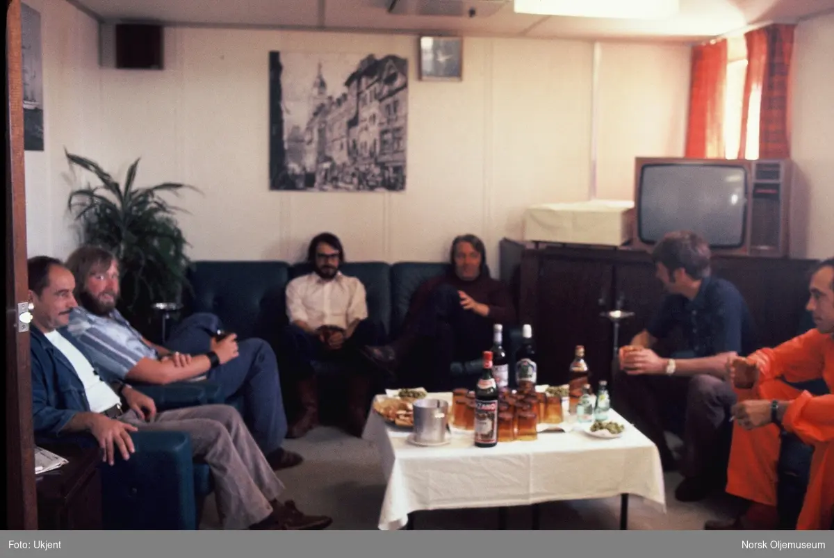Seks menn slapper av i en tv-stue på en plattform eller et fartøy. På bordet står drikkevarer. Arne Vingerhagen fra Statoil sitter helt til høyre.