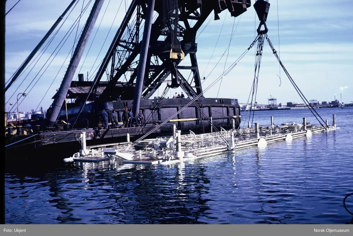 En stor modul for reparasjon av rør under vann dras etter taubåt fra et stort havneanlegg.
